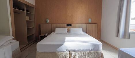 A hotel room with a large bed, a wardrobe, a bedside table with a phone, and a window with curtains.