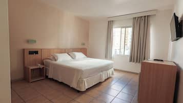 Habitación de hotel con cama, mesita de noche, escritorio, televisor y ventana con cortinas.