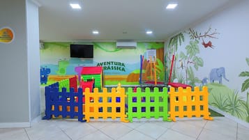 Zona de juegos infantiles con estructuras coloridas y un mural que representa una escena de selva.