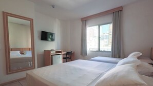 Habitación de hotel con dos camas, un escritorio, una silla, un televisor y una ventana con cortinas.