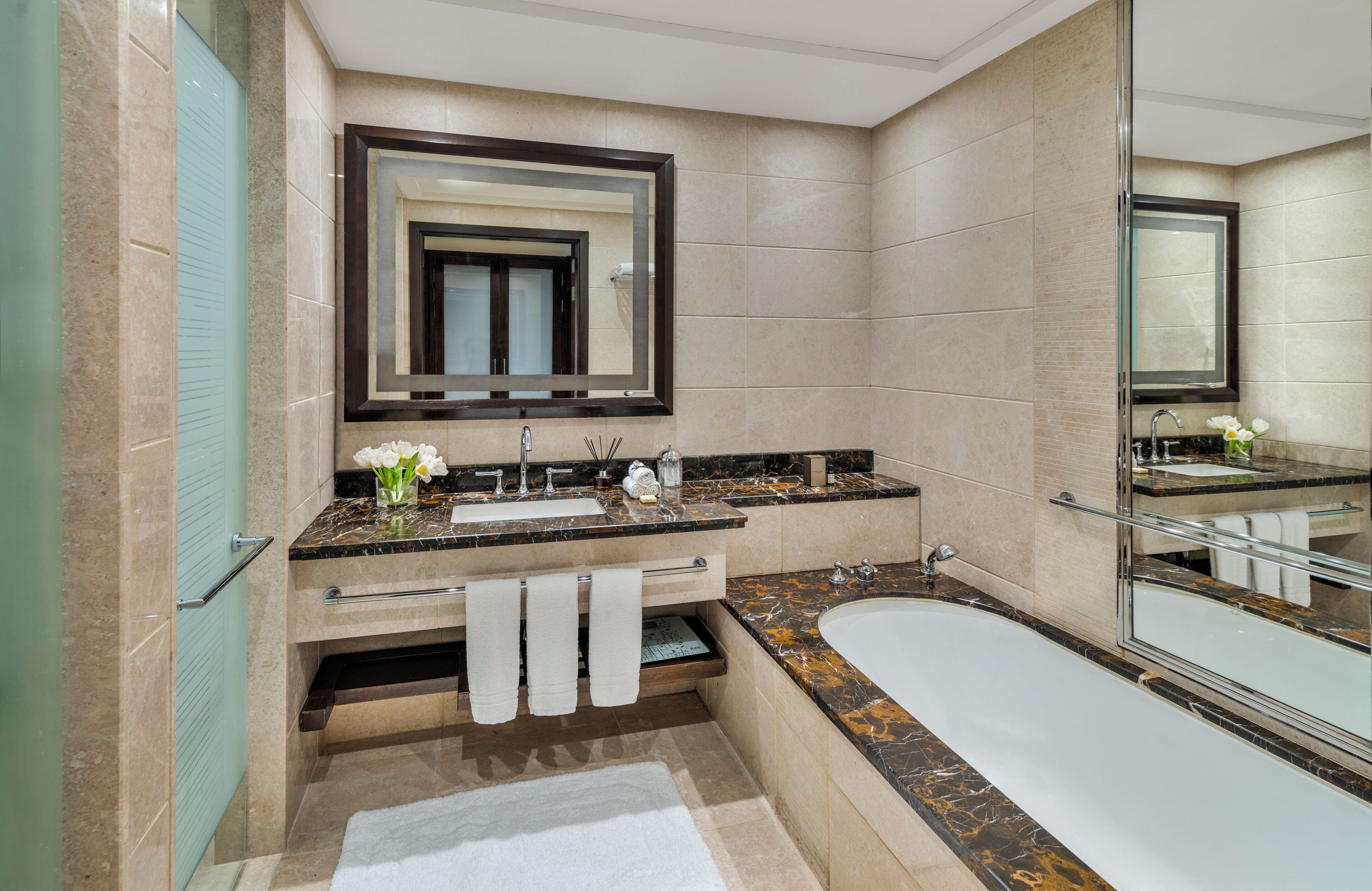A modern bathroom with a marble sink, a large mirror, a bathtub, and a glass shower enclosure.