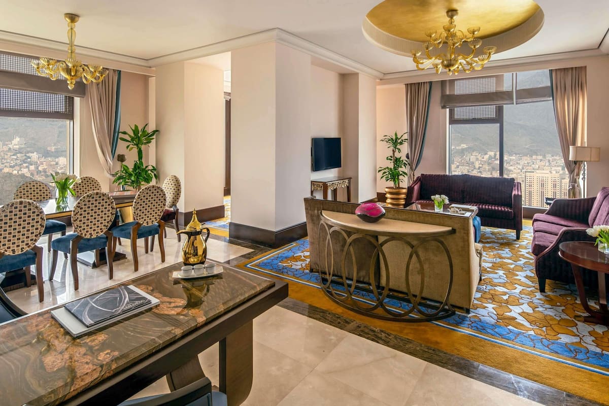 A hotel room with a dining area, a sofa, a TV, and a view of the city.