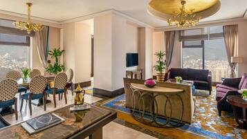 Quarto de hotel com área de refeições, sofá, televisão e vista para a cidade.