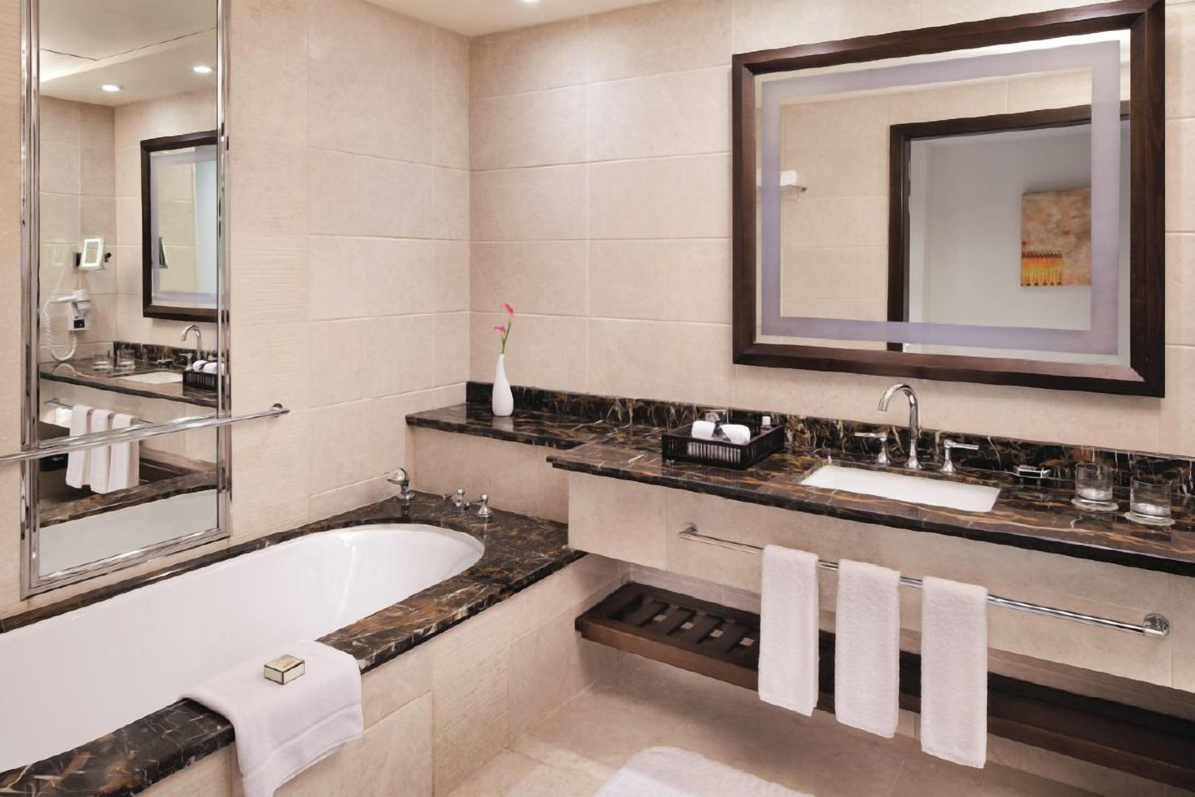 A modern bathroom with a marble bathtub, a large mirror, and a vanity with a sink and towel rack.