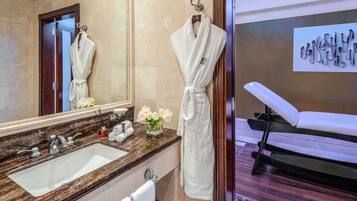 Une salle de bain avec un lavabo en marbre, un miroir, un peignoir suspendu à un crochet et un fauteuil de massage.