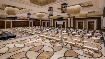 Un salón de conferencias amplio con filas de mesas y sillas, un escenario y un suelo estampado.