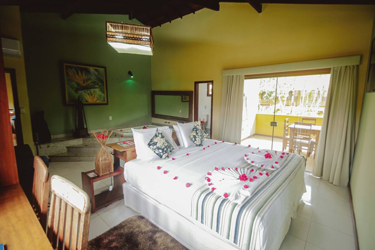 A bedroom with a bed, a TV, a dining area, and a balcony.