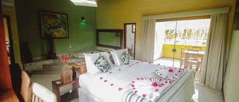 Un dormitorio con cama, televisor, zona de comedor y balcón.