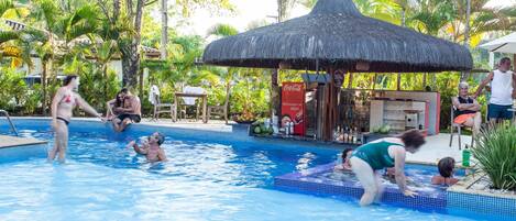 A swimming pool with a thatched roof structure, surrounded by lush greenery and palm trees.