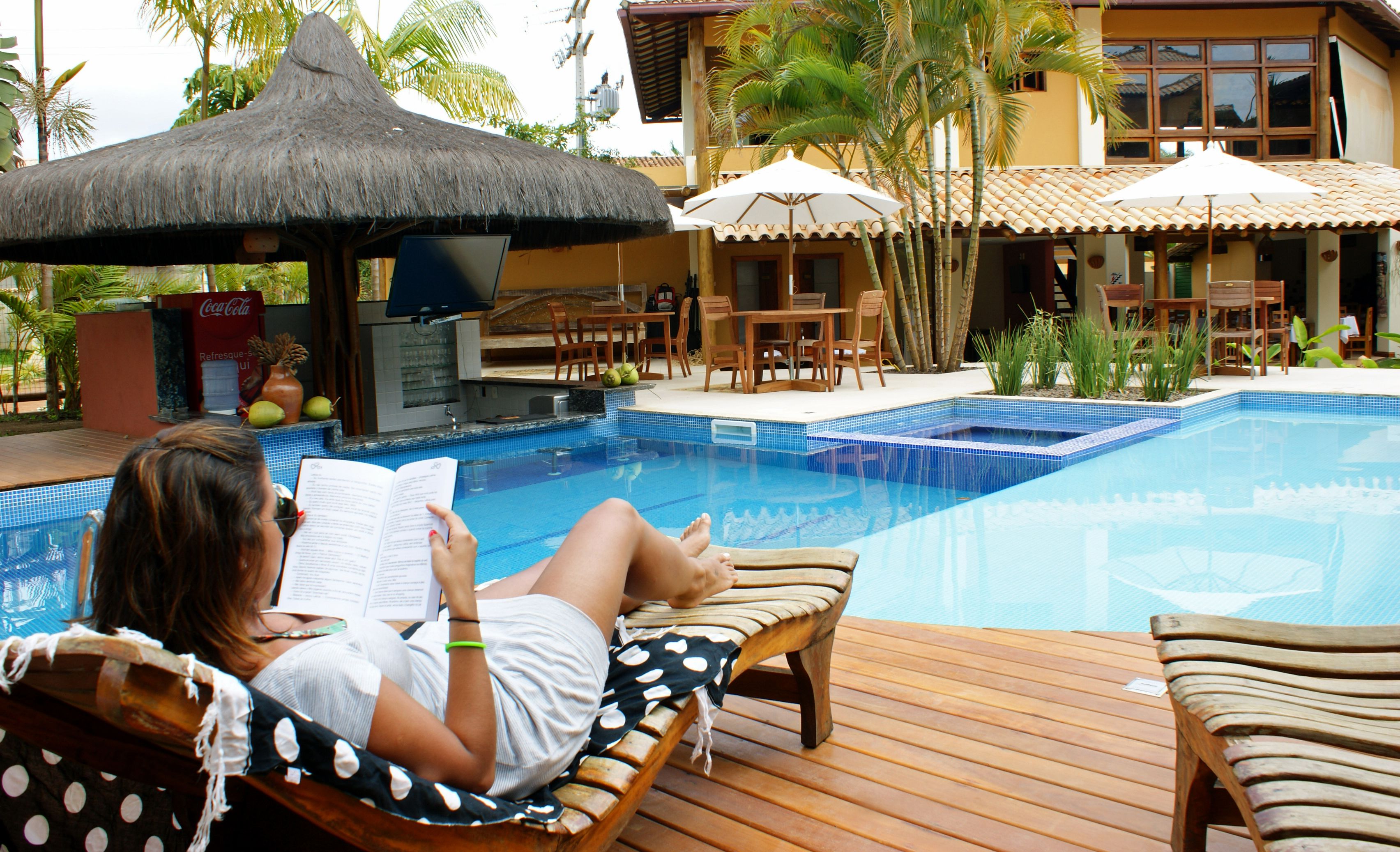 A woman relaxing by a poolside lounge chair, reading a book.
