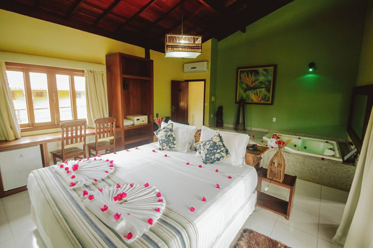 A hotel room with a bed, a desk, a chair, a bathtub, and a green wall.