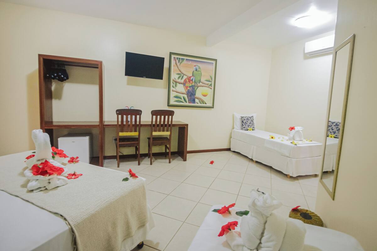 A hotel room with two beds, a small table, chairs, a TV, a painting, and a mirror.