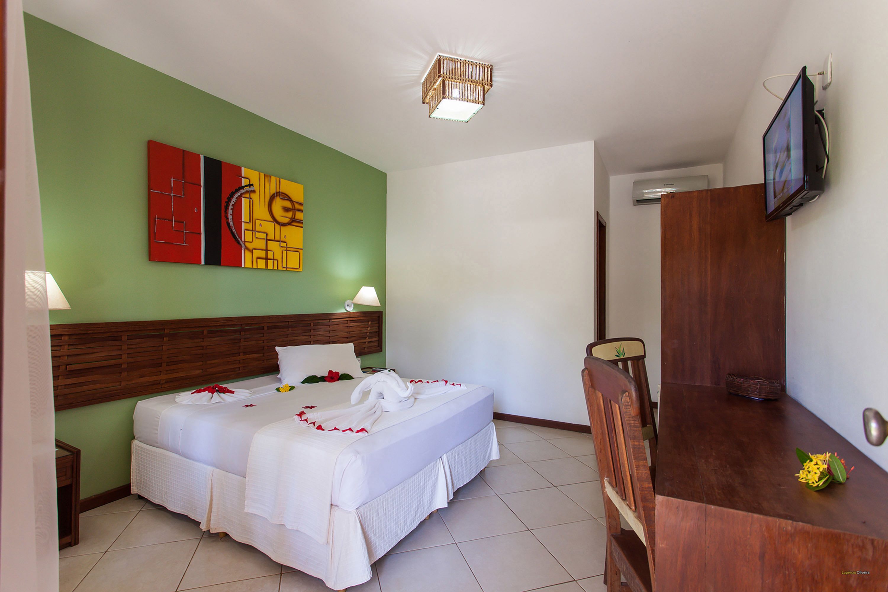 Ein Hotelzimmer mit einem hölzernen Kopfteil, einem Bett mit weißer Bettwäsche, einem an der Wand befestigten Fernseher und einer grünen Akzentwand.