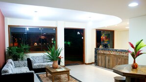 A modern living room with a sofa, a coffee table, and a dining table. There are potted plants and a view of the outside. - Pousada Pedra Torta (Itacaré)