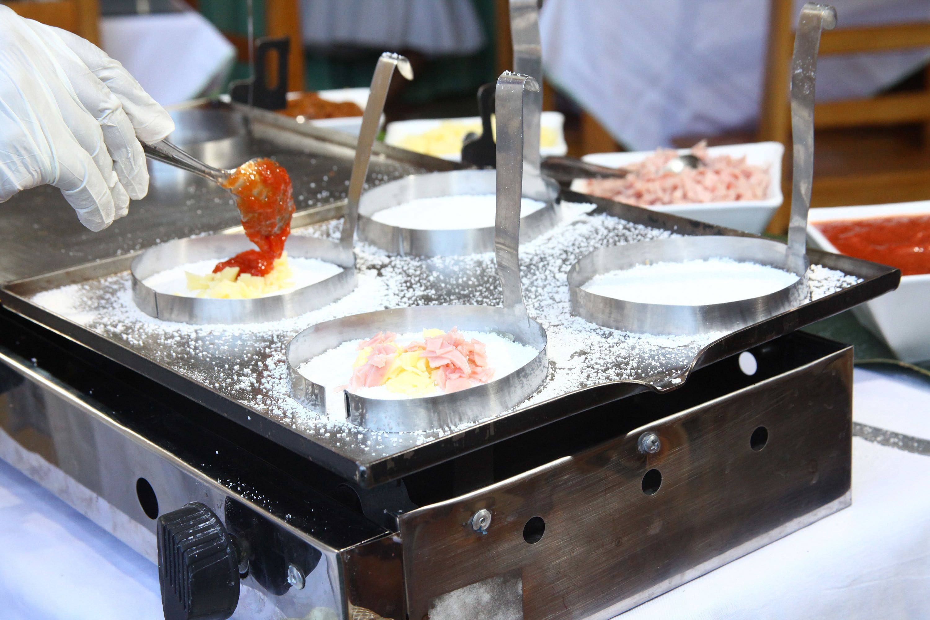 Una zona de preparación de alimentos con una superficie metálica y tres recipientes redondos, uno de ellos con una cucharada de comida.