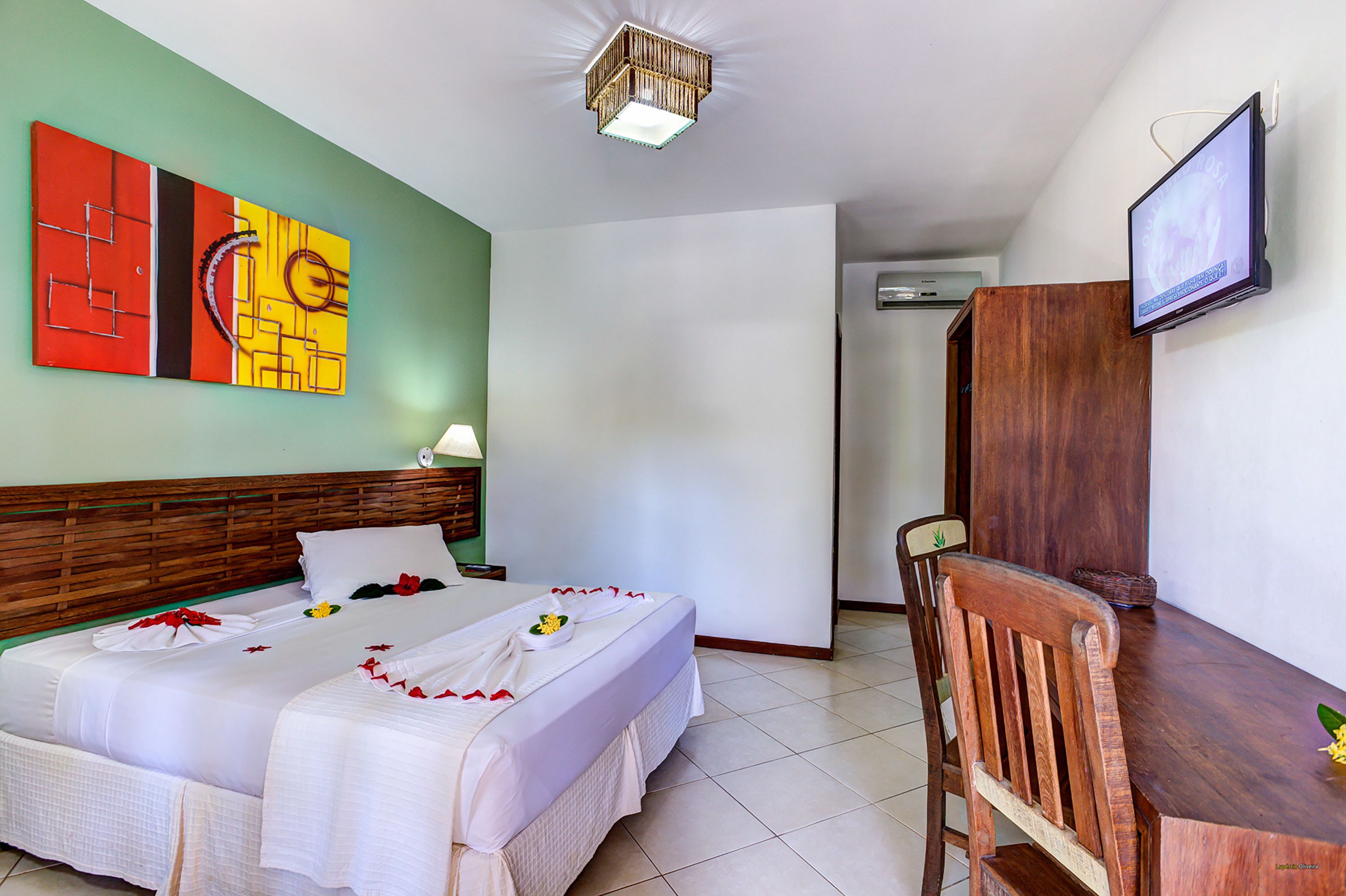 A hotel room with a bed, a desk, a TV, and a painting on the wall.