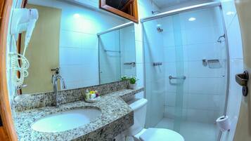 Une salle de bain dotée d’un lavabo avec un plan de toilette en granit, d’un miroir, d’un sèche-cheveux, de toilettes et d’une douche à parois de verre.
