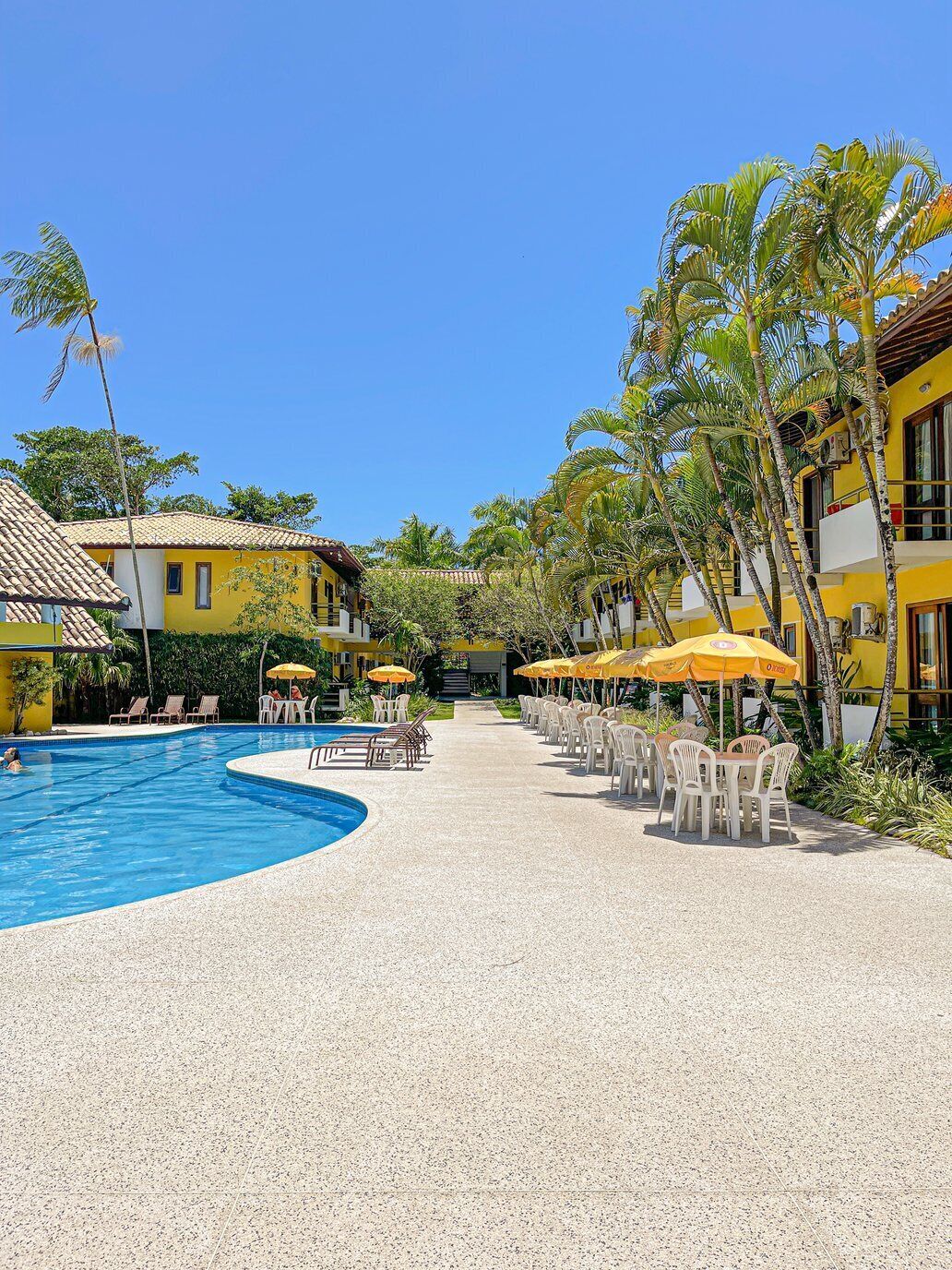 Een resort met een zwembad, terras en palmbomen.