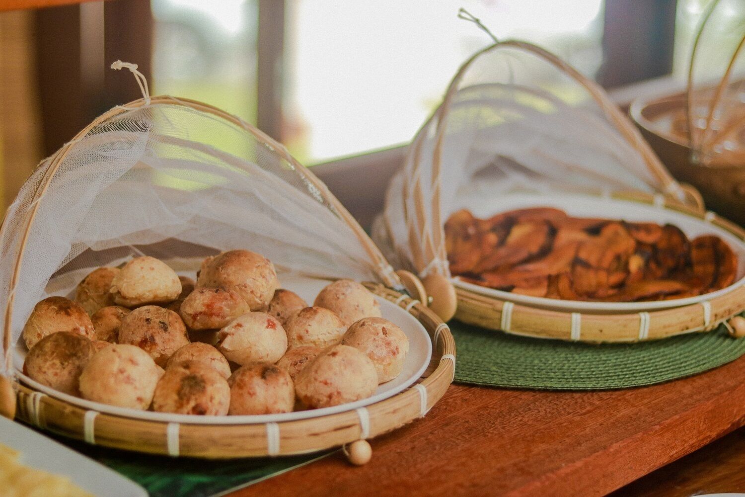 Two woven baskets on a wooden table, one containing round pastries and the other containing flat, baked goods.