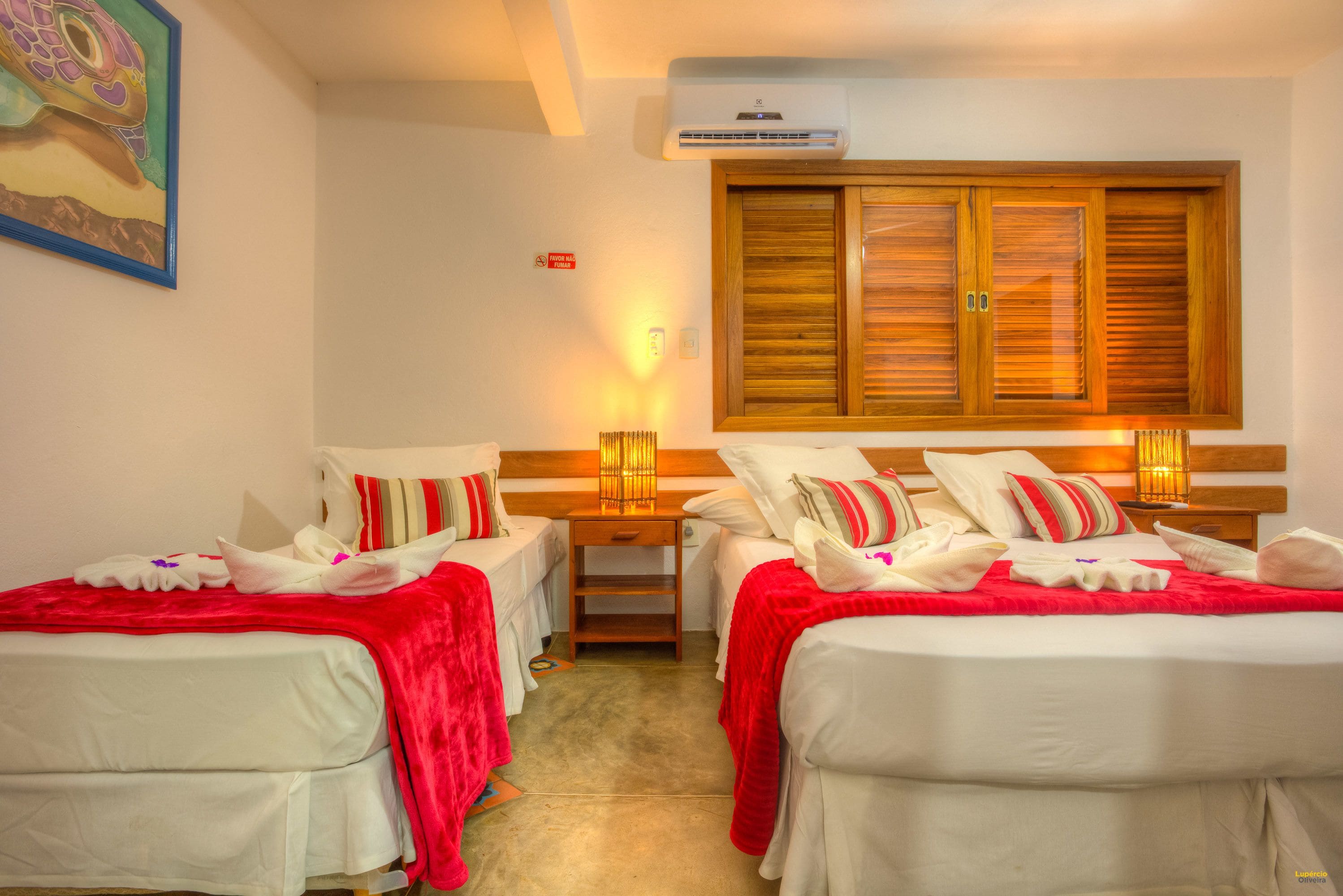 A hotel room with two beds, each with white linens and red blankets, a wooden headboard, and a wall-mounted air conditioner.