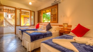 Une chambre d’hôtel avec trois lits, un ventilateur de plafond, un appareil de climatisation, une fenêtre donnant sur des palmiers et un escalier menant à un espace extérieur.