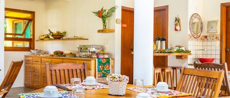 A dining area with a wooden table set for four, surrounded by chairs, and a kitchen area with wooden cabinets and a hanging plant.