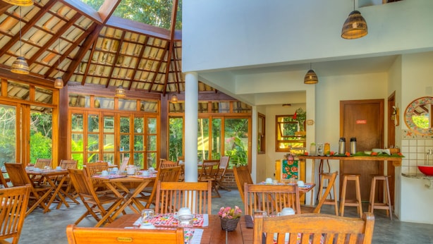 Un vaste espace de salle à manger avec des tables et des chaises en bois, de grandes fenêtres et un coin cuisine visible au fond.