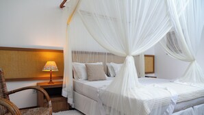 A bedroom with a four-poster bed, a bedside lamp, and a wicker chair. - Sarana Praia Hotel (Porto Seguro)