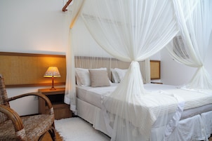 Quarto com cama de dossel, luminária de cabeceira e cadeira de vime.