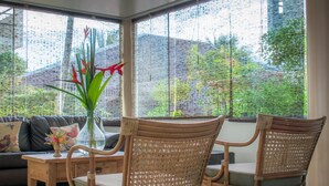A room with a large window, wicker chairs, a wooden table, and a sofa. - Sarana Praia Hotel (Porto Seguro)