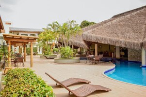 Un área junto a la piscina con sillones de descanso, una estructura con techo de paja y una alberca.