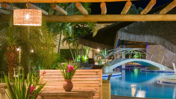 A pool area with a wooden bench, a thatched roof, and a hanging light fixture. - Sarana Praia Hotel (Porto Seguro)