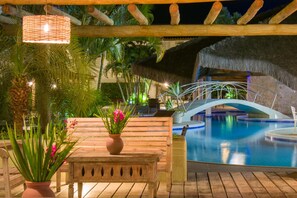 A pool area with a wooden bench, a thatched roof, and a hanging light fixture. - Sarana Praia Hotel (Porto Seguro)