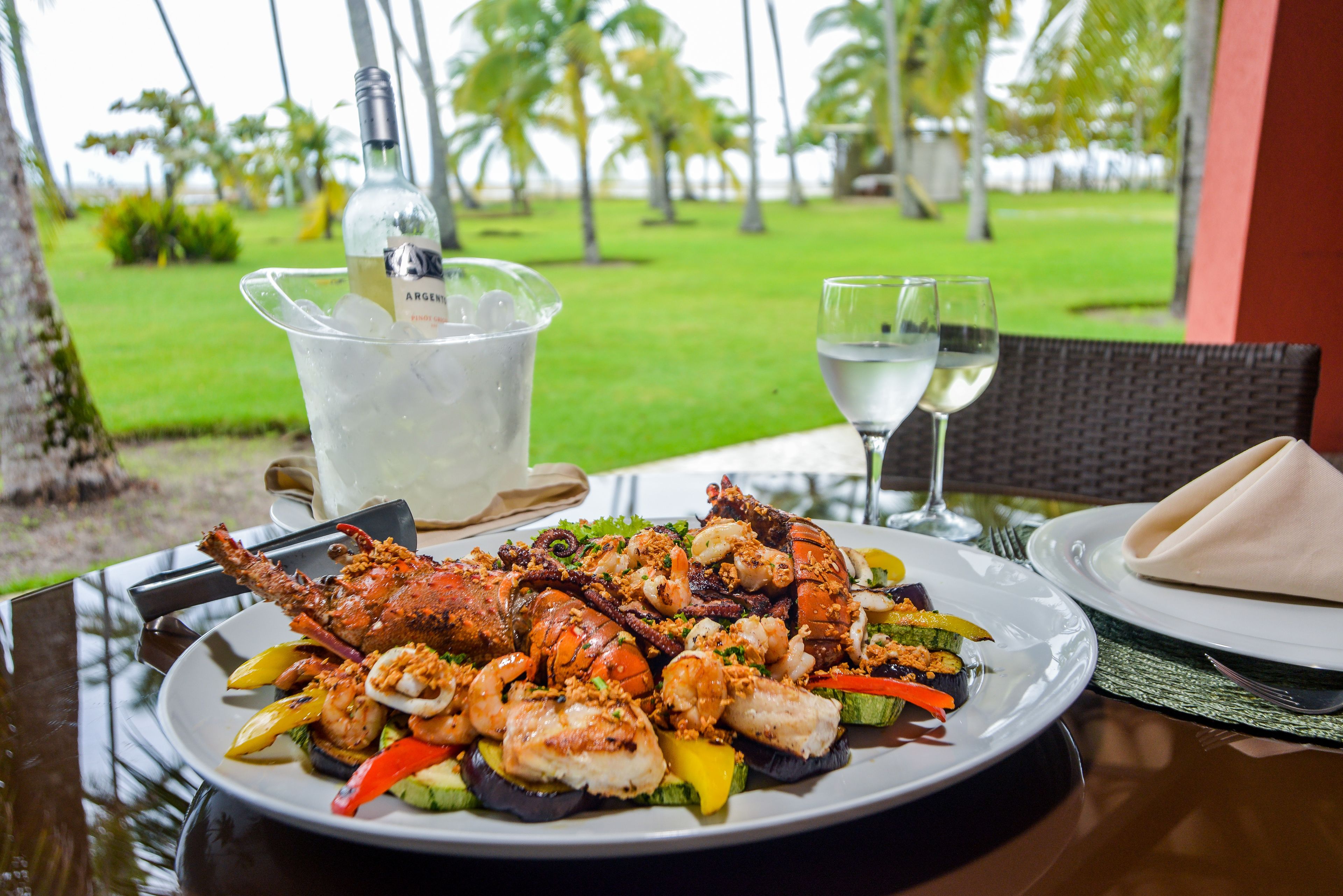 Una mesa de comedor con un plato de mariscos, una botella de vino blanco y un vaso de agua.