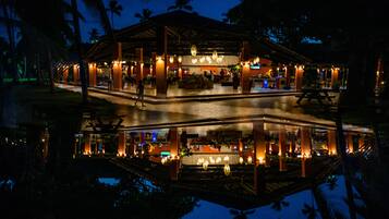 A two-story building with a covered outdoor area, a pool, and palm trees.
