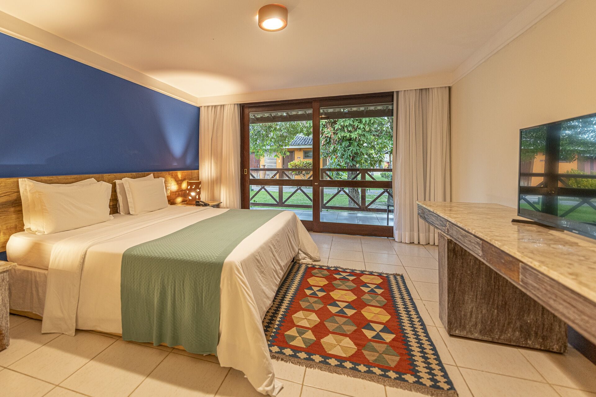 A hotel room with a bed, a desk, a TV, and a view of the outdoors.
