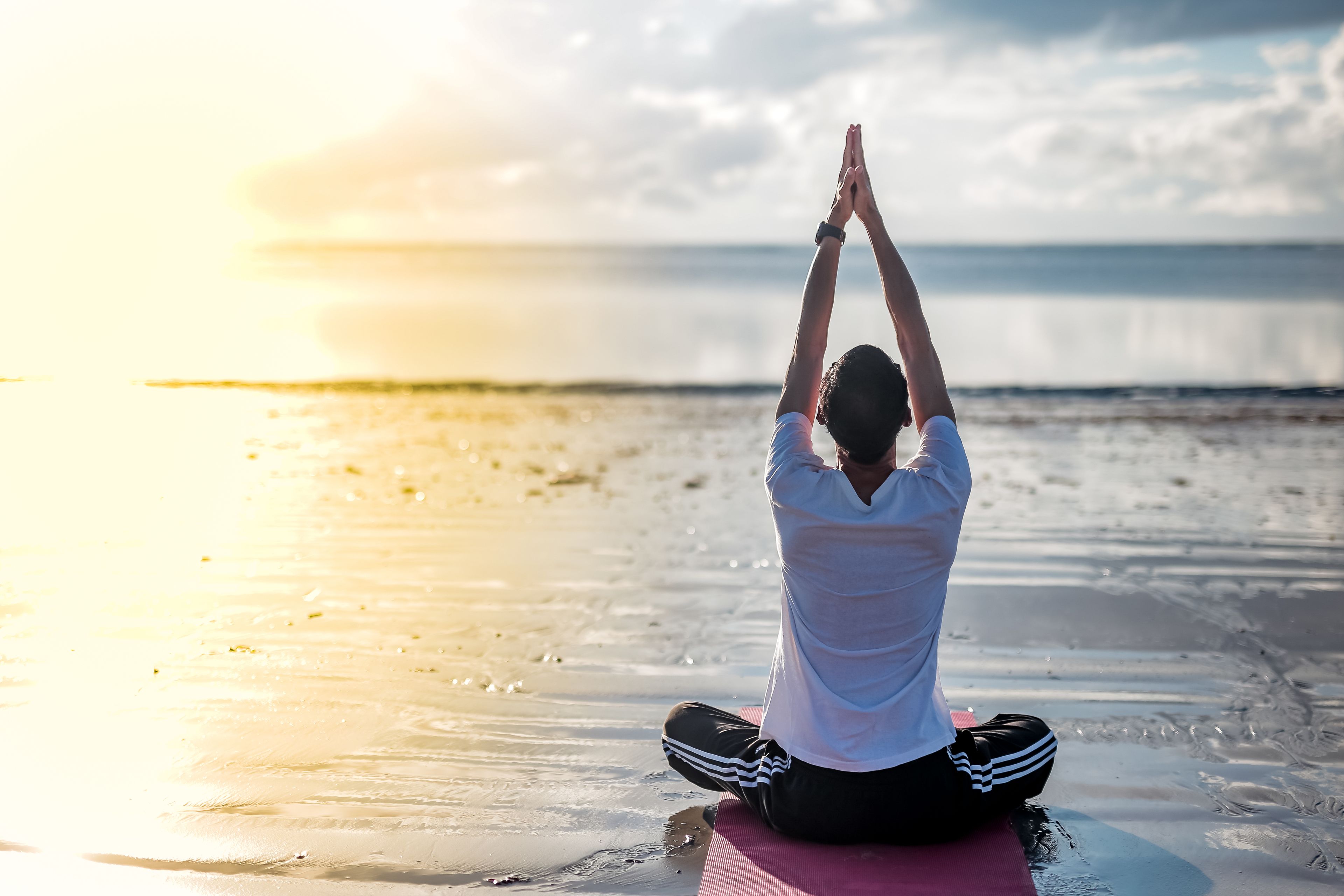 A person sitting on a yoga mat on a beach at sunset.