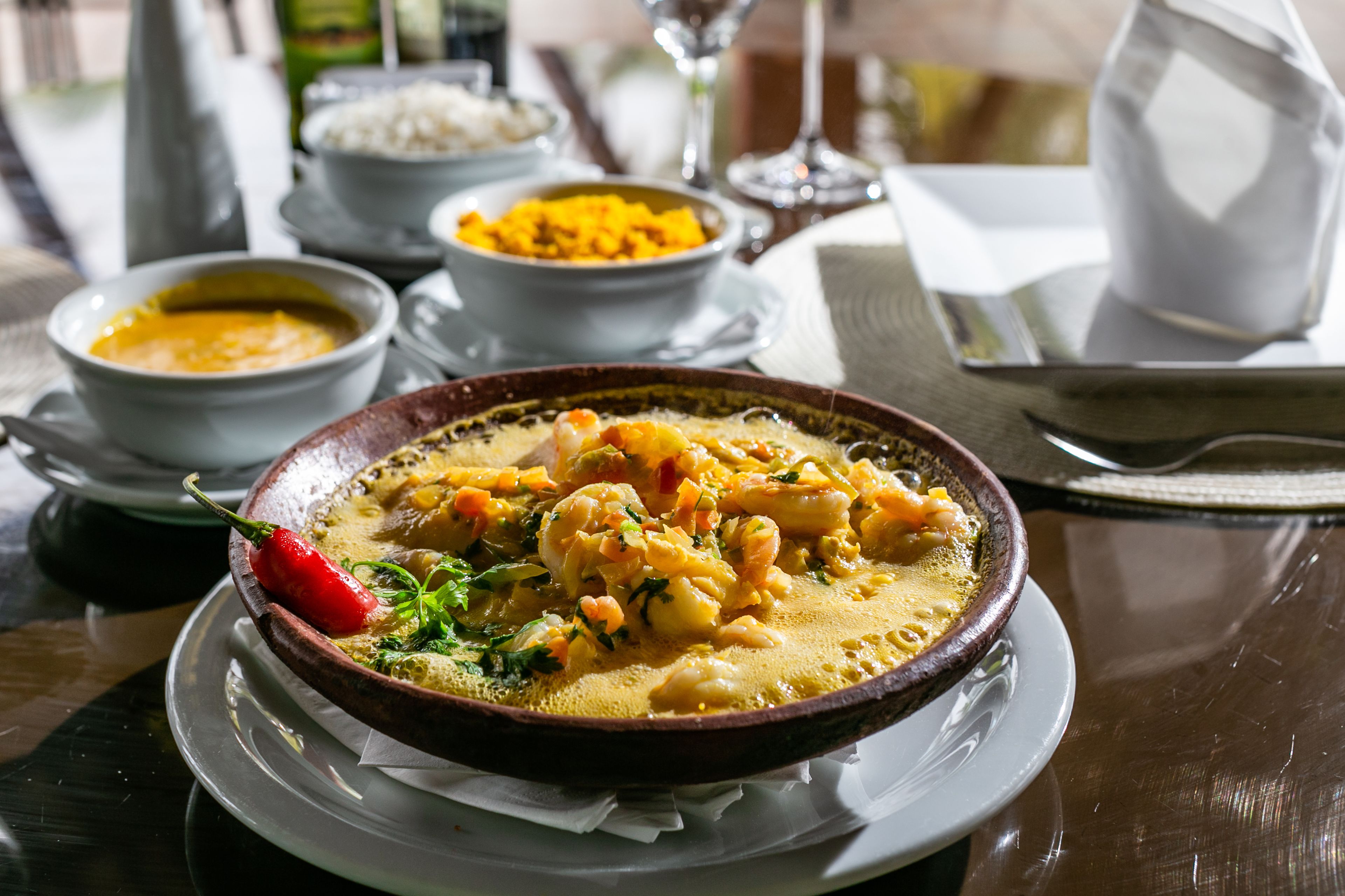 Uma mesa com um prato de curry, um pimentão vermelho e um copo de água.