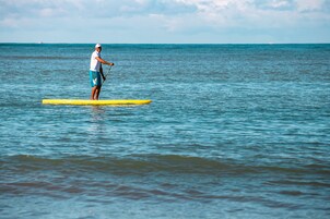A person standing on a yellow paddleboard in calm ocean waters.