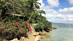 A coastal beach with clear water, rocky shore, and lush greenery. - Hotel Portaló (Cairu)