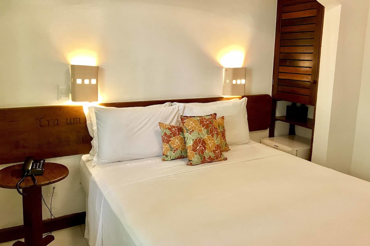 A hotel room with a bed, two wall-mounted lamps, a telephone, and a wooden headboard.