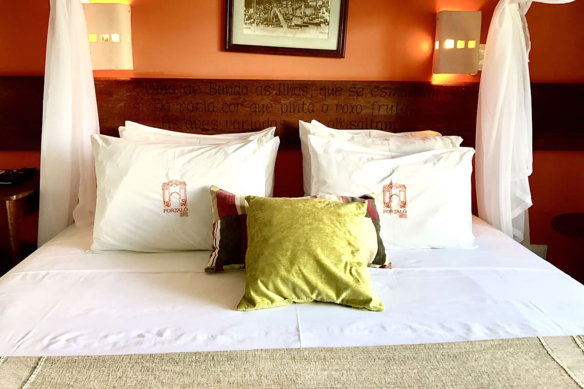 A hotel room with a bed, white pillows, a green pillow, and a framed picture on the wall.
