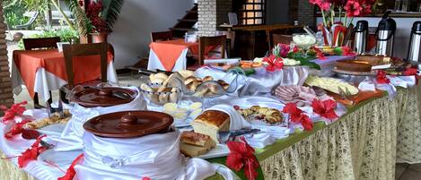 A buffet table with various food items and decorations, including hibiscus flowers and a view of a staircase and a brick wall.