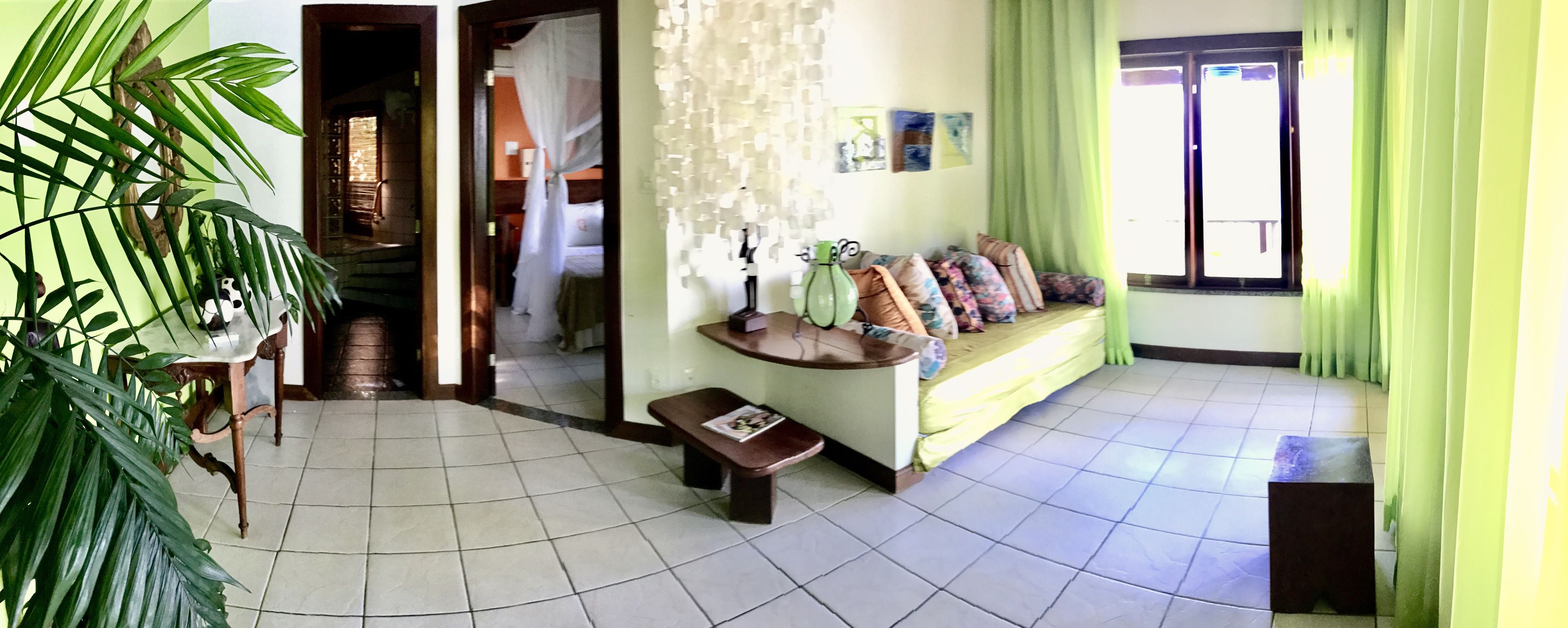 A room with a tiled floor, a bench, a sofa with cushions, a green plant, and a window with curtains.