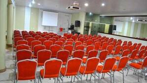 Un salón de conferencias con filas de sillas anaranjadas, una pantalla de proyector y una pizarra.