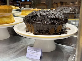 Un pastel de chocolate sobre un plato blanco, con un cartel que dice 'Bolo de Chocolate'.