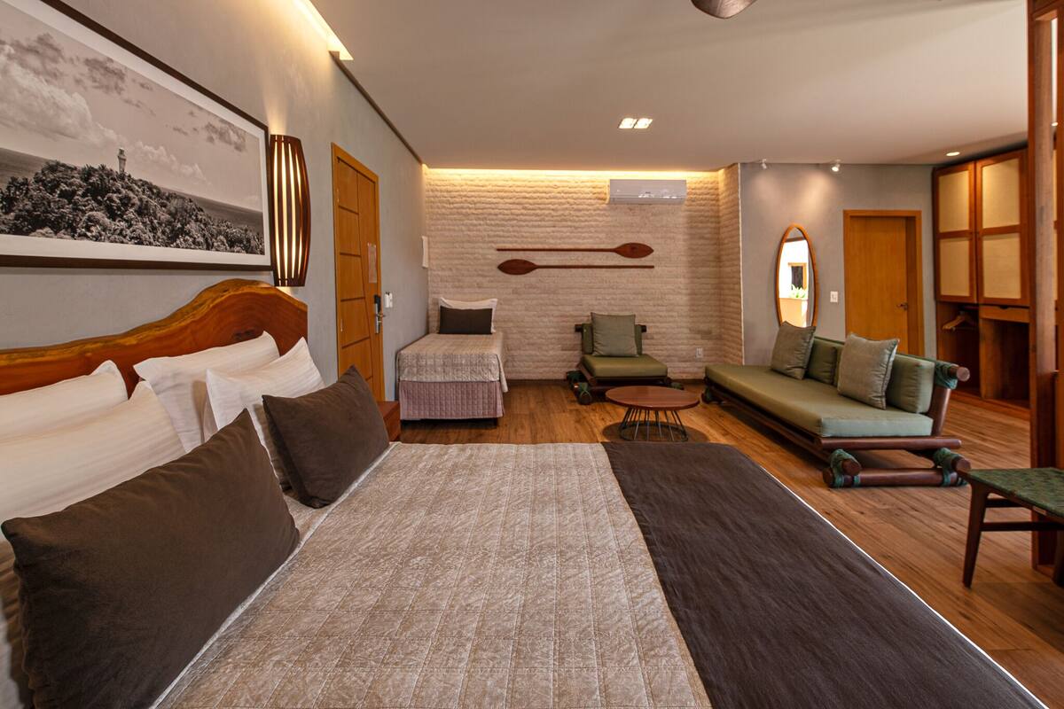 Een hotelkamer met een groot bed, een bank, een kleine tafel en een stoel. Er hangt een spiegel en een fotolijst aan de muur.