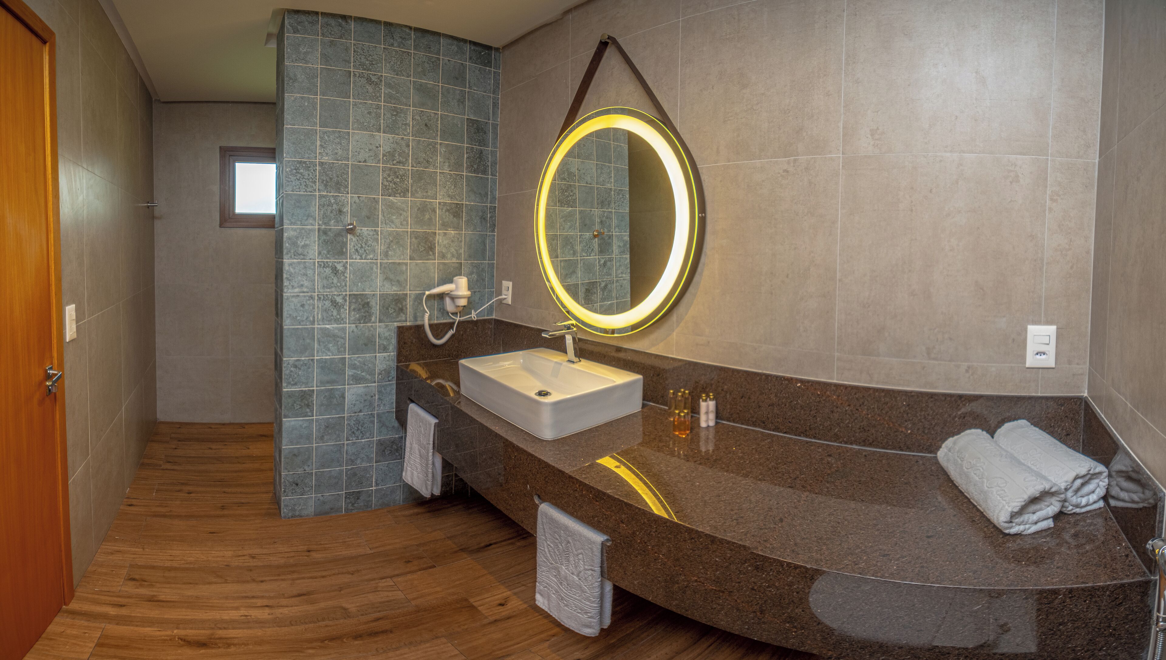 A modern bathroom with a curved vanity, a round mirror with illuminated edges, and a wooden floor.