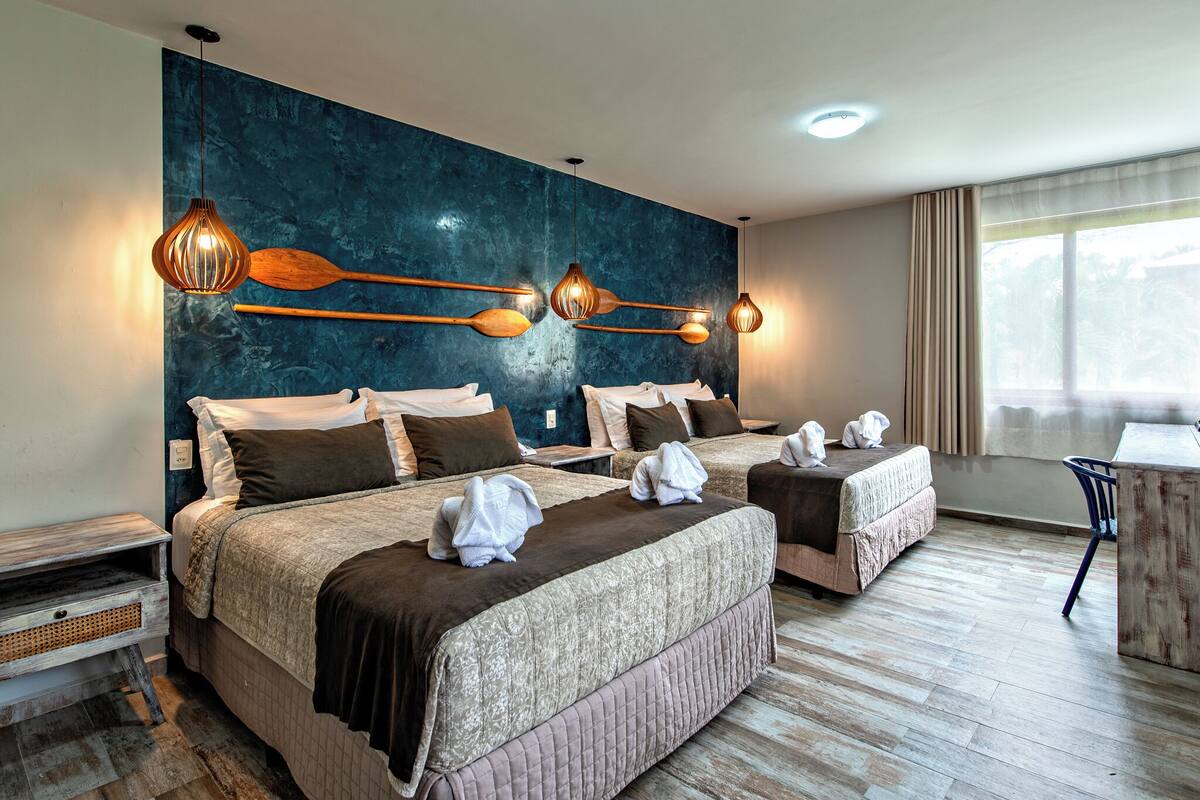 Een hotelkamer met twee bedden, een houten nachtkastje, een bureau en een groot raam met gordijnen.