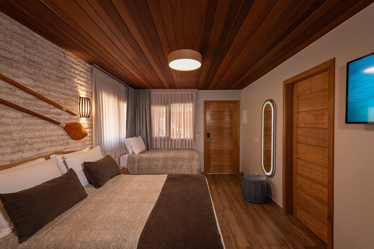Een hotelkamer met een houten plafond, een bakstenen muur, een bed met hoofdeinde, een nachtkastje, een spiegel en een televisie.